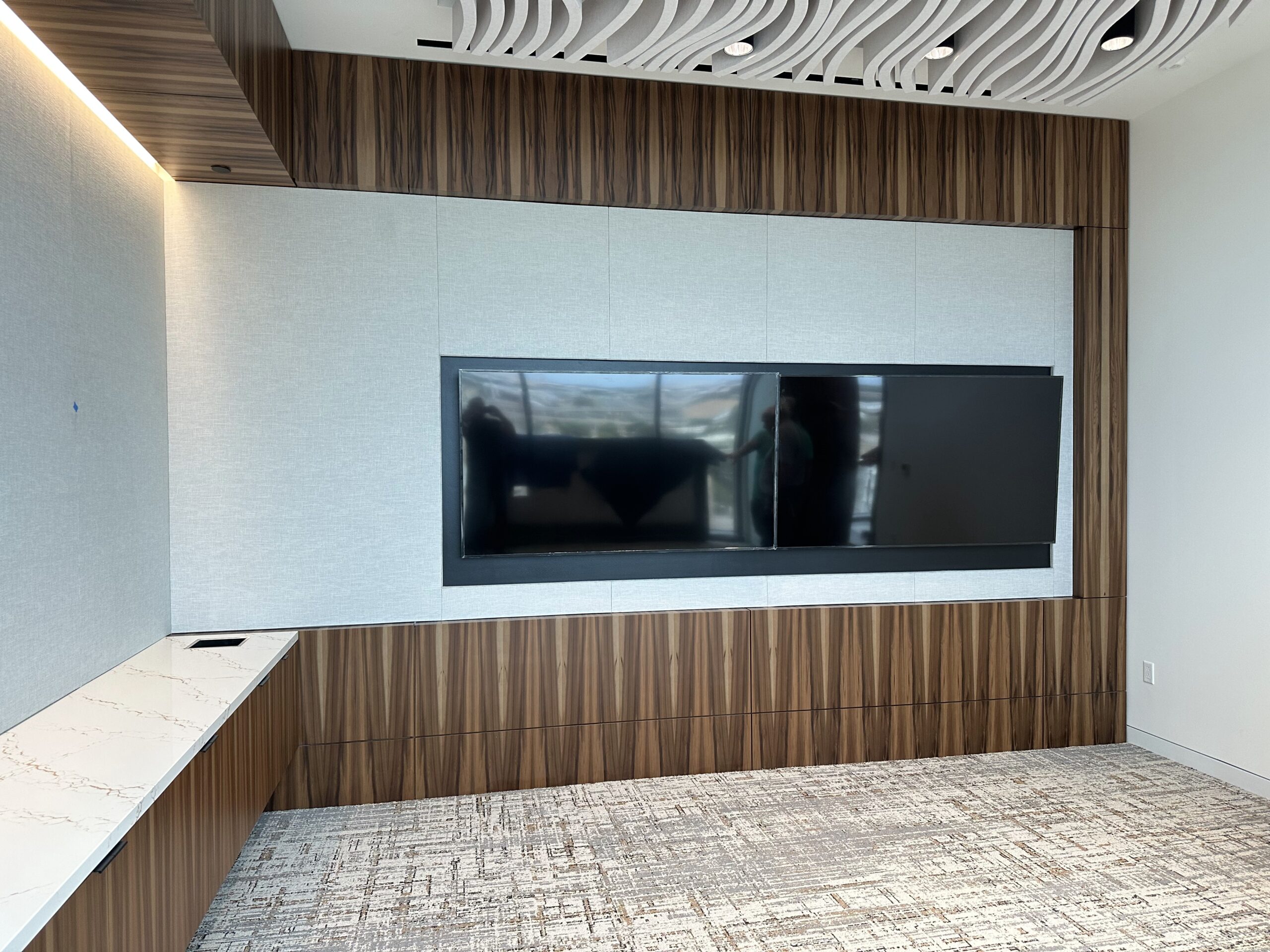 Modern conference room featuring a large dual-screen display mounted on a textured wall, complemented by sleek wooden cabinetry and a minimalist design.